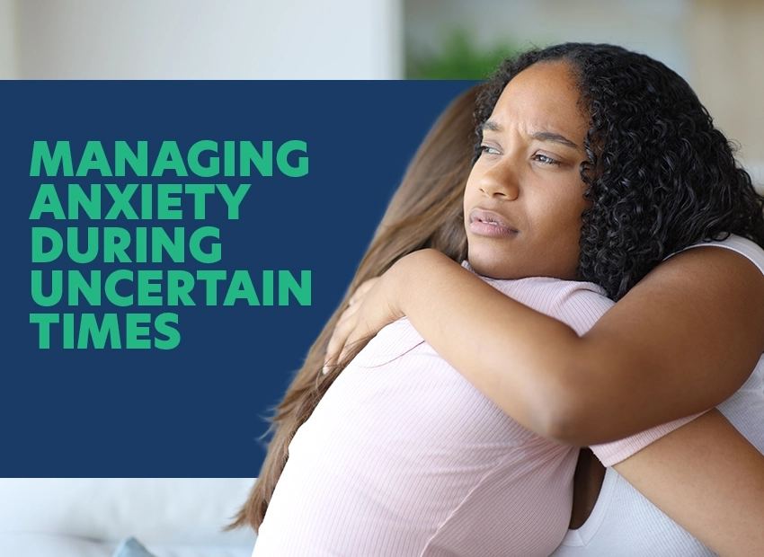 Young woman hugging her knees with a worried expression, beside text reading Managing Anxiety During Uncertain Times