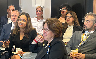 Group of Optimus Health Care staff and community members attentively listening during a professional meeting or event.